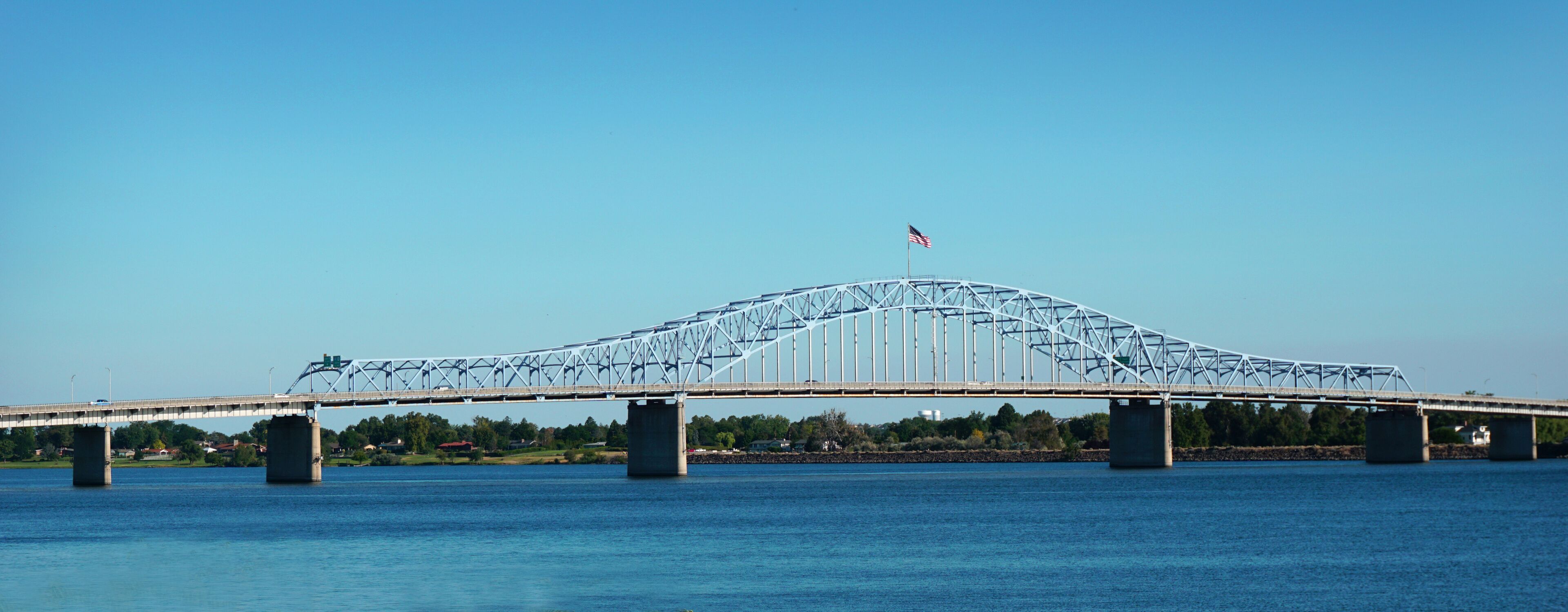 A large steel bridge spanning a river with a flag on top.