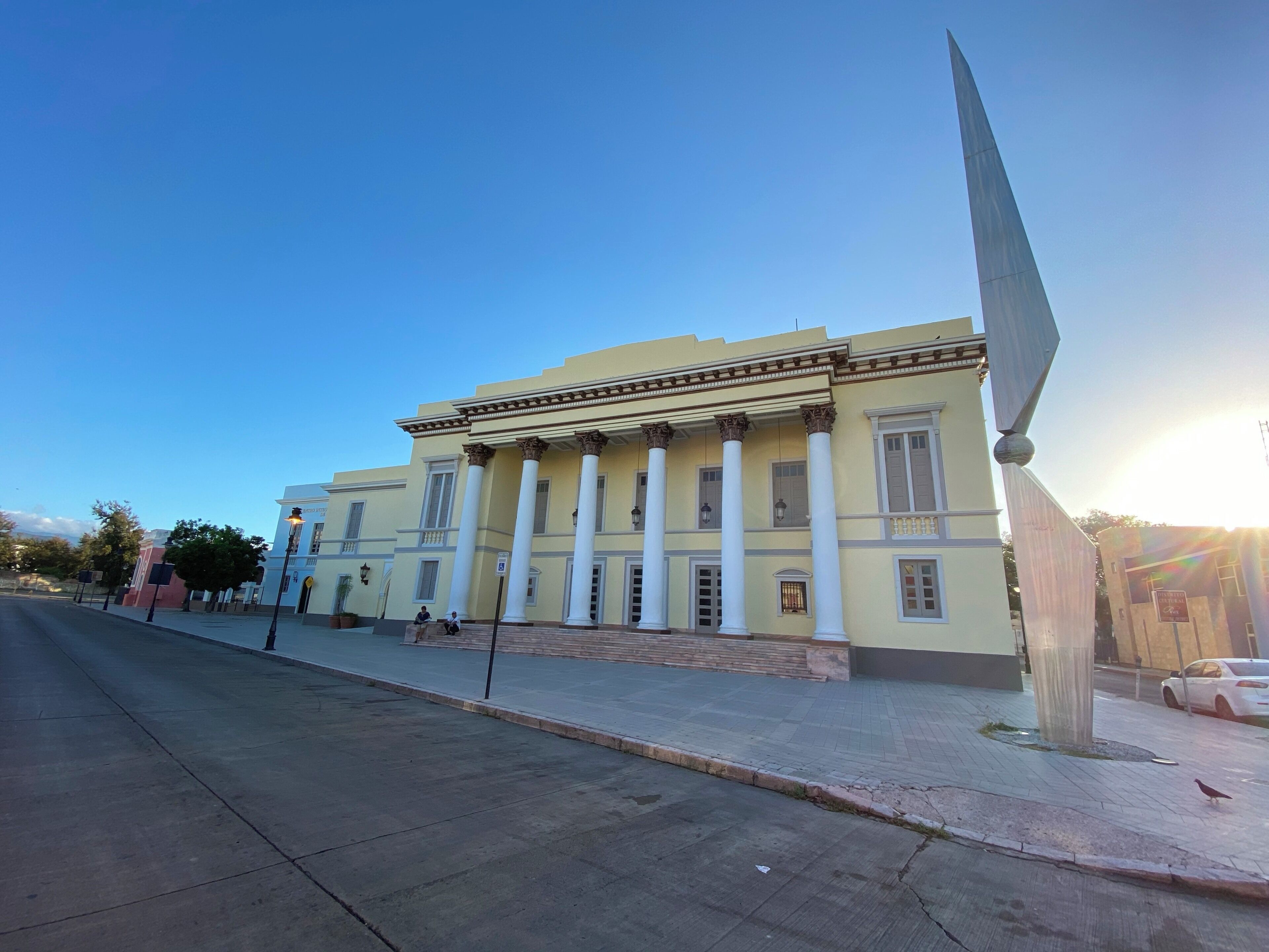 A classical building with columns and a large sculpture on the sidewalk.