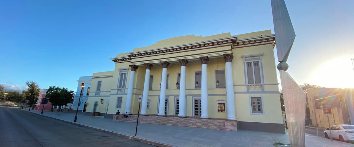 A classical building with columns and a large sculpture on the sidewalk.