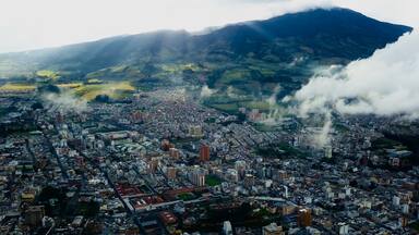 A cityscape with a mountain in the background and smoke rising from buildings.