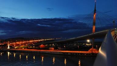A nighttime view of a bridge with lights reflecting on the water.
