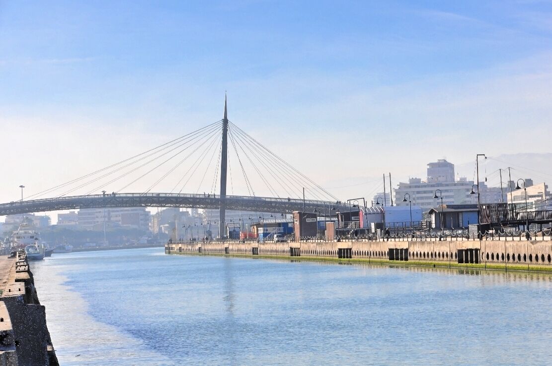 A cable-stayed bridge over a river with industrial buildings in the background.
