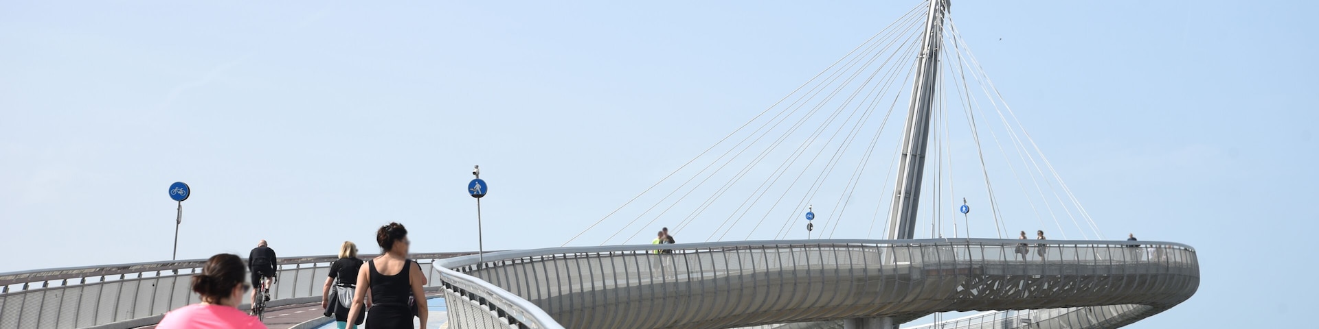 A pedestrian bridge with a cable-stayed design, a blue walkway, and a view of the sea.