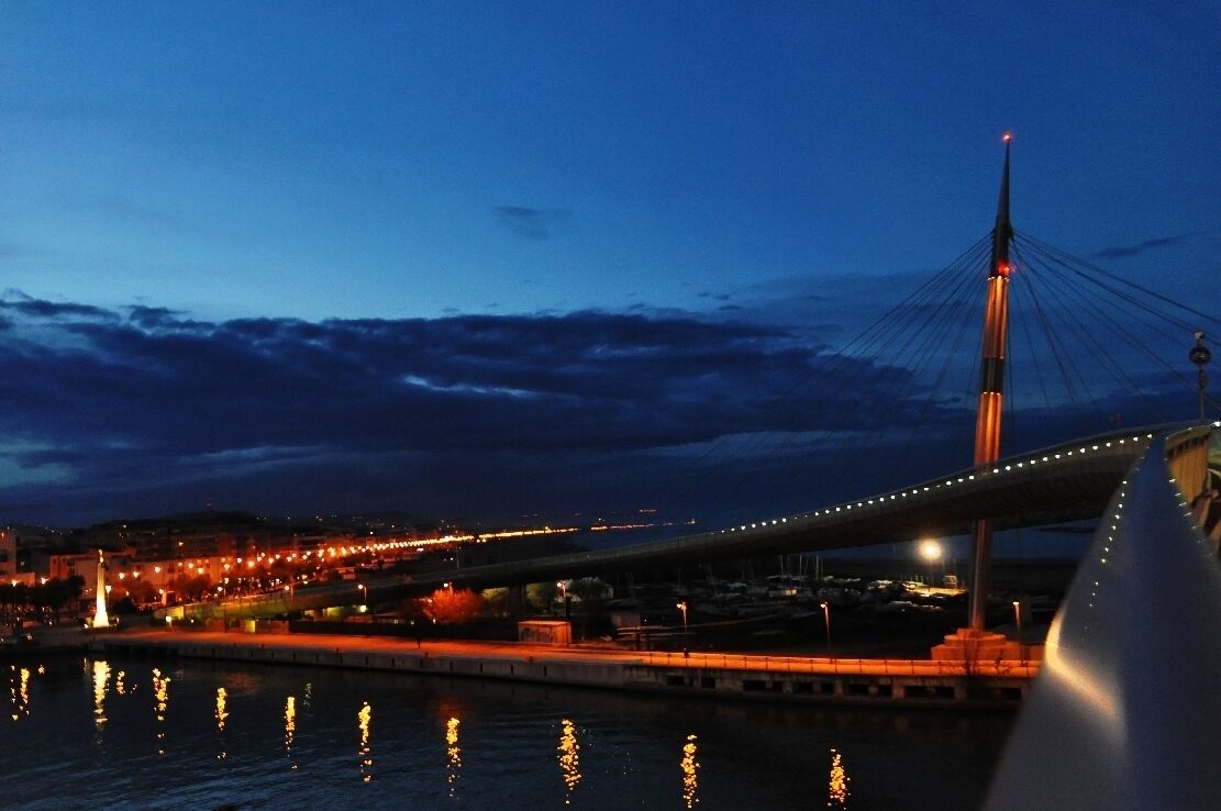 A nighttime view of a bridge with lights reflecting on the water.
