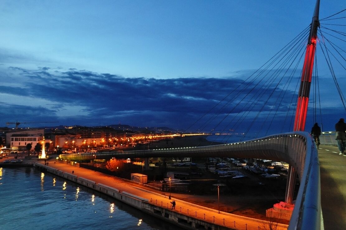 A cable-stayed bridge at dusk with city lights reflecting on the water.