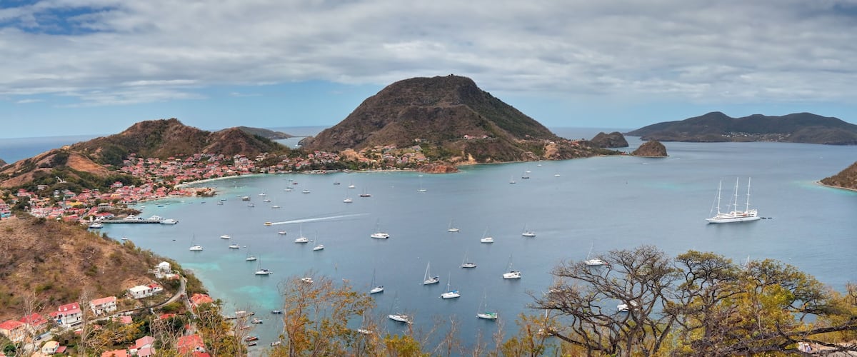 A coastal town with a mountain, clear blue waters, and numerous boats.