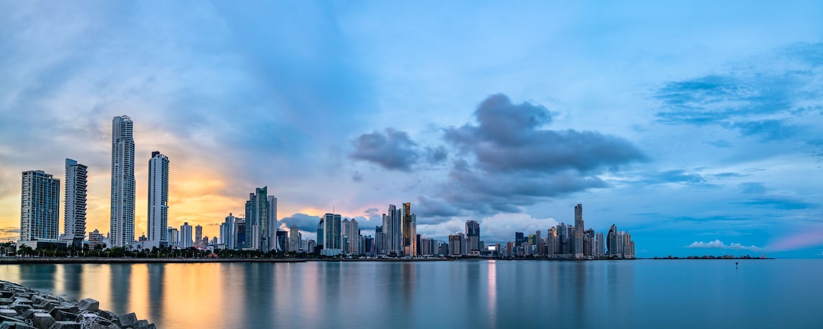 A city skyline with high-rise buildings, a calm waterfront, and a sunset sky.