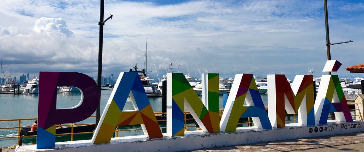 A colorful sign spelling "PANAMÁ" with a marina and boats in the background.