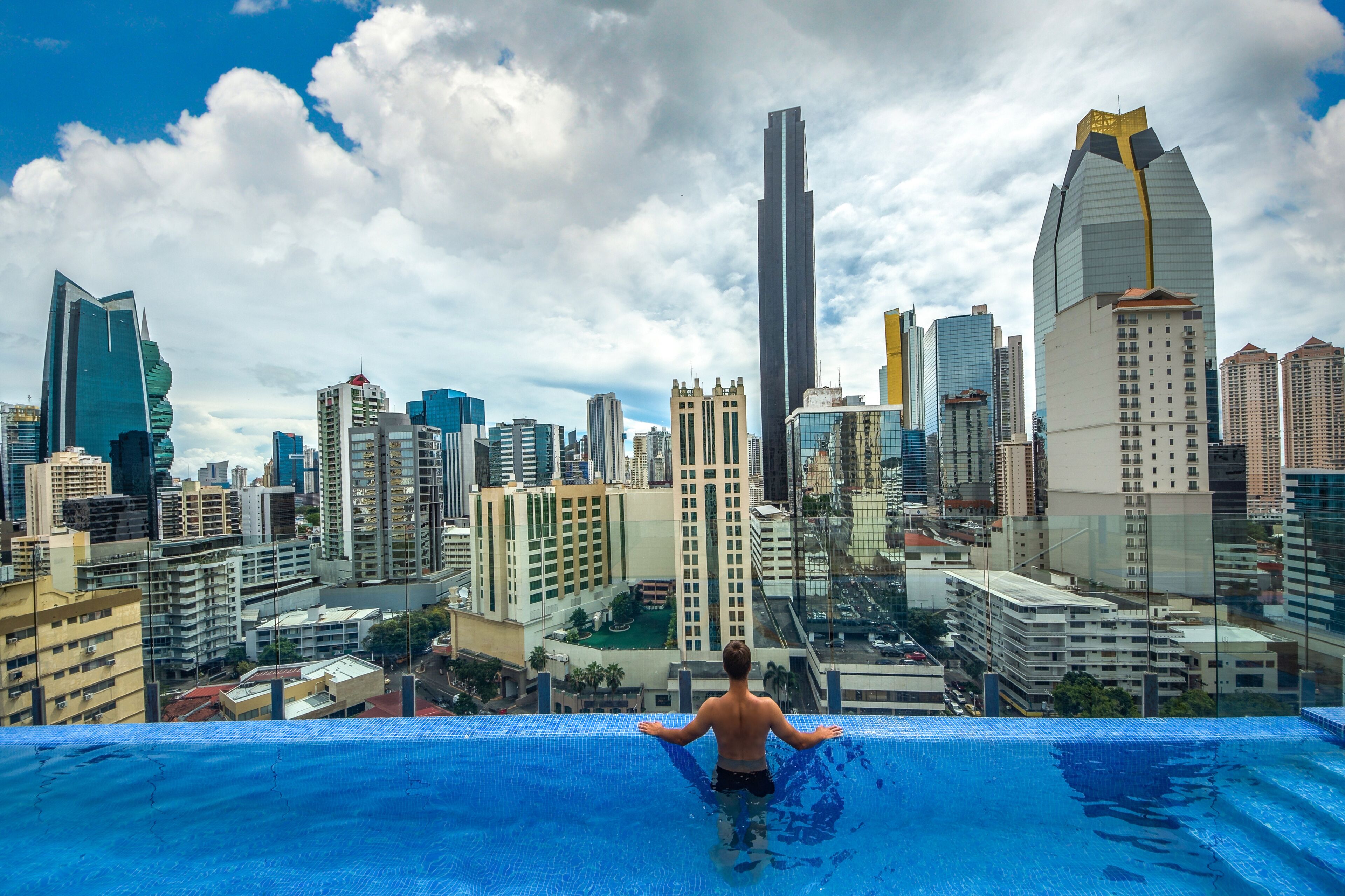 Un paisaje urbano con modernos rascacielos y una persona de pie al borde de una piscina.