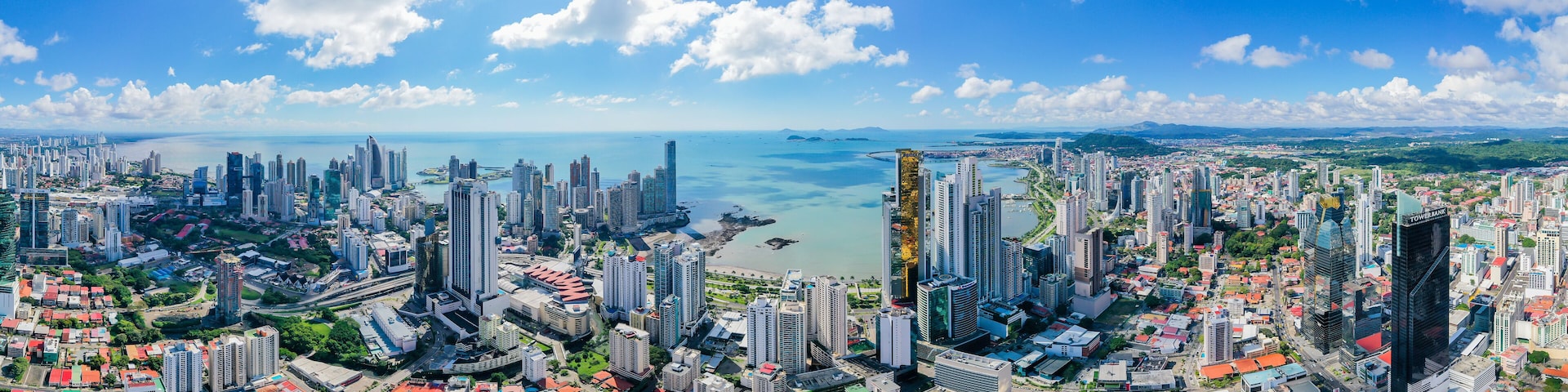 A coastal cityscape with high-rise buildings, a marina, and a clear blue sky.