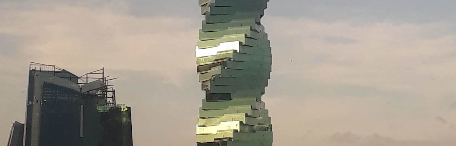 Um arranha-céu moderno e espiral com um design único, rodeado por outros edifícios em um ambiente urbano.