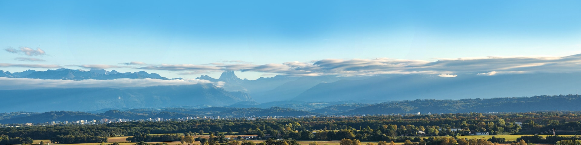 A mountainous landscape with a town in the foreground and a prominent peak in the background.