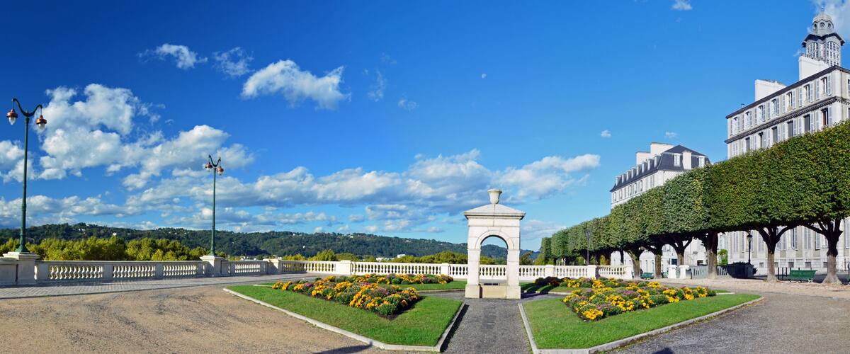 Ein angelegter Garten mit einem zentralen Denkmal, einem weißen Zaun und einem großen Gebäude mit einer Kuppel.