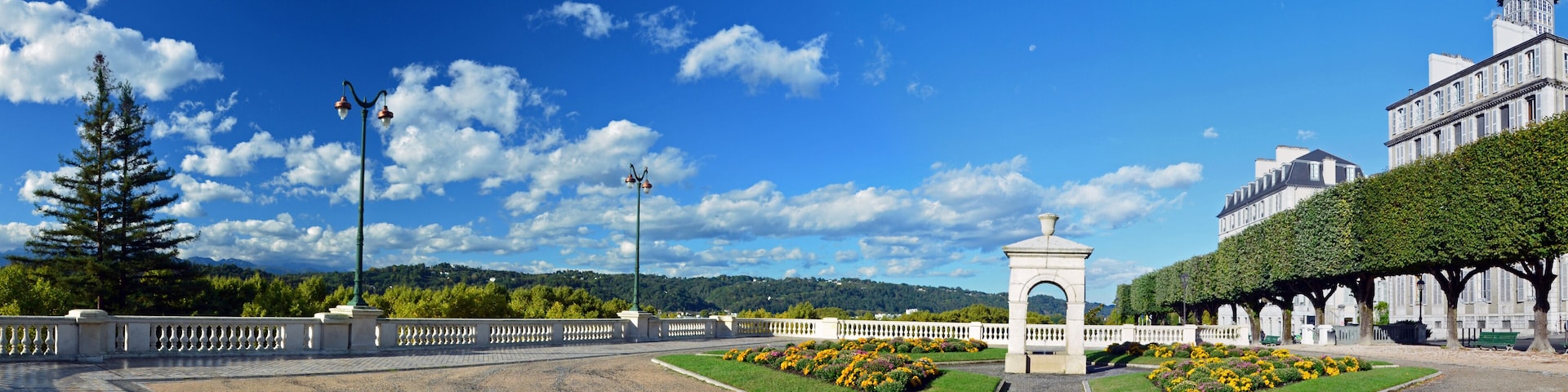 Un jardín ajardinado con un monumento central, una valla blanca y un edificio grande con una cúpula.