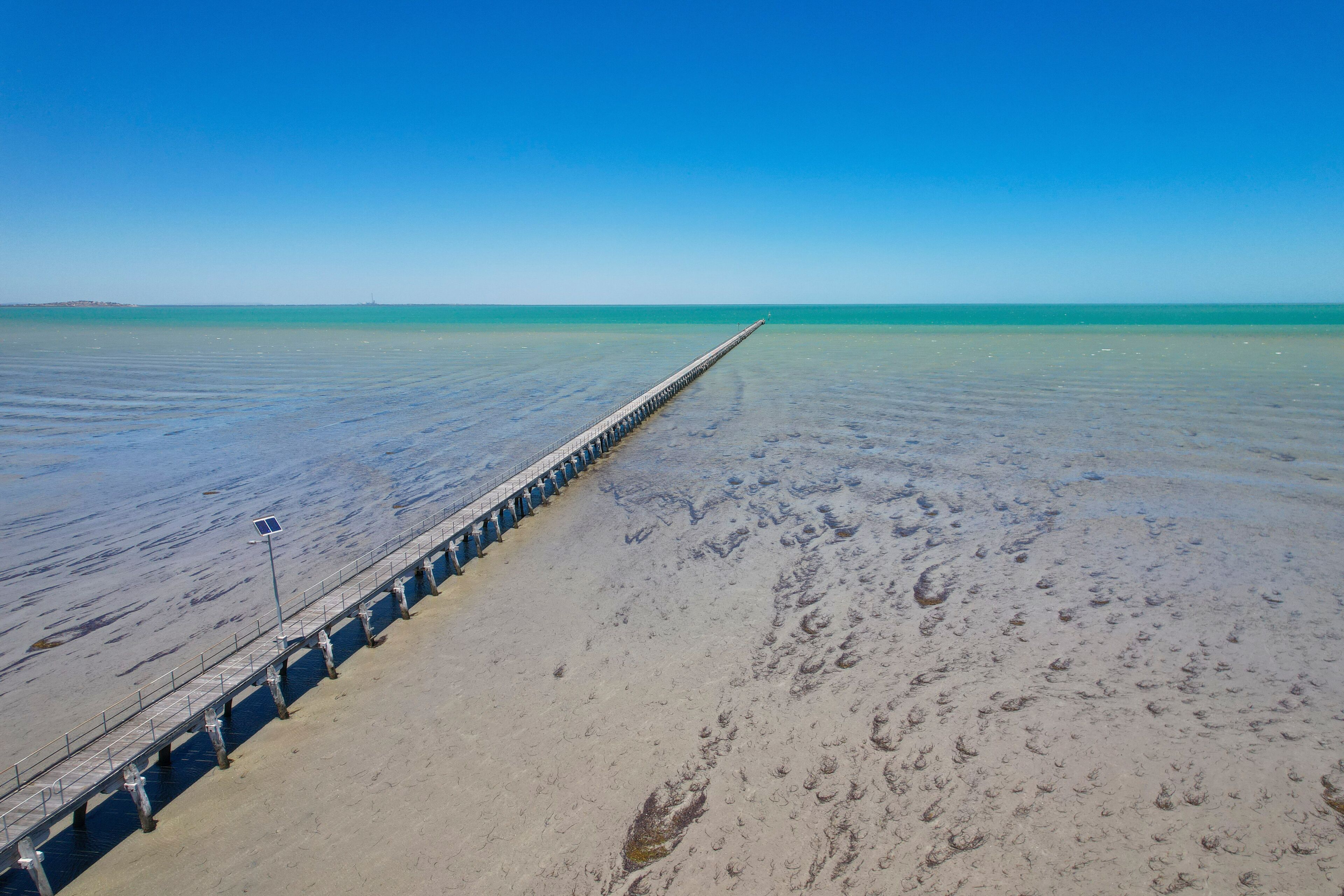 Aerial view of tranquil Germein Bay with the longest jetty under a blue sky, Port Germein, Australia.