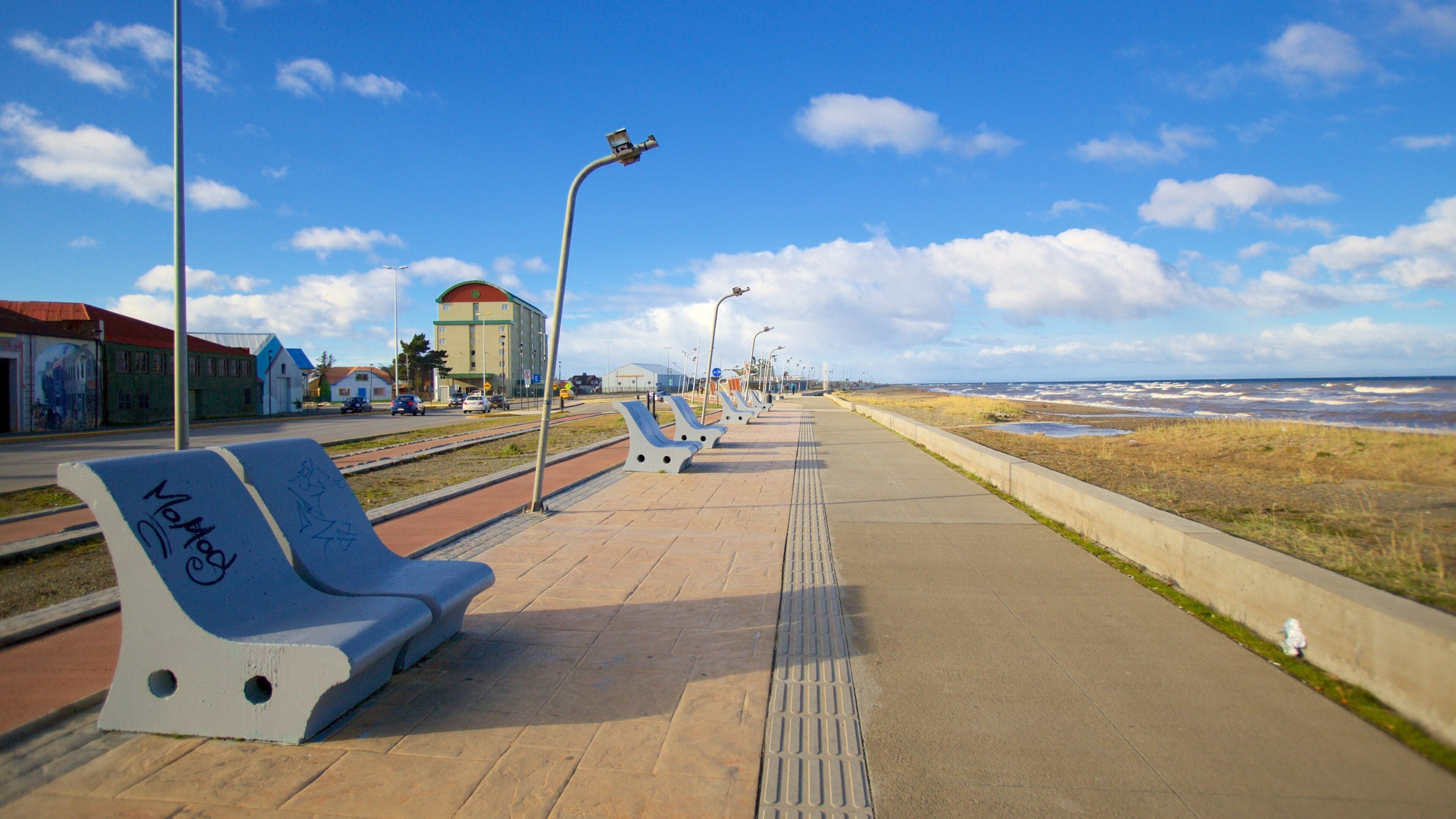 Un paseo marítimo con bancos, farolas y vista al mar.