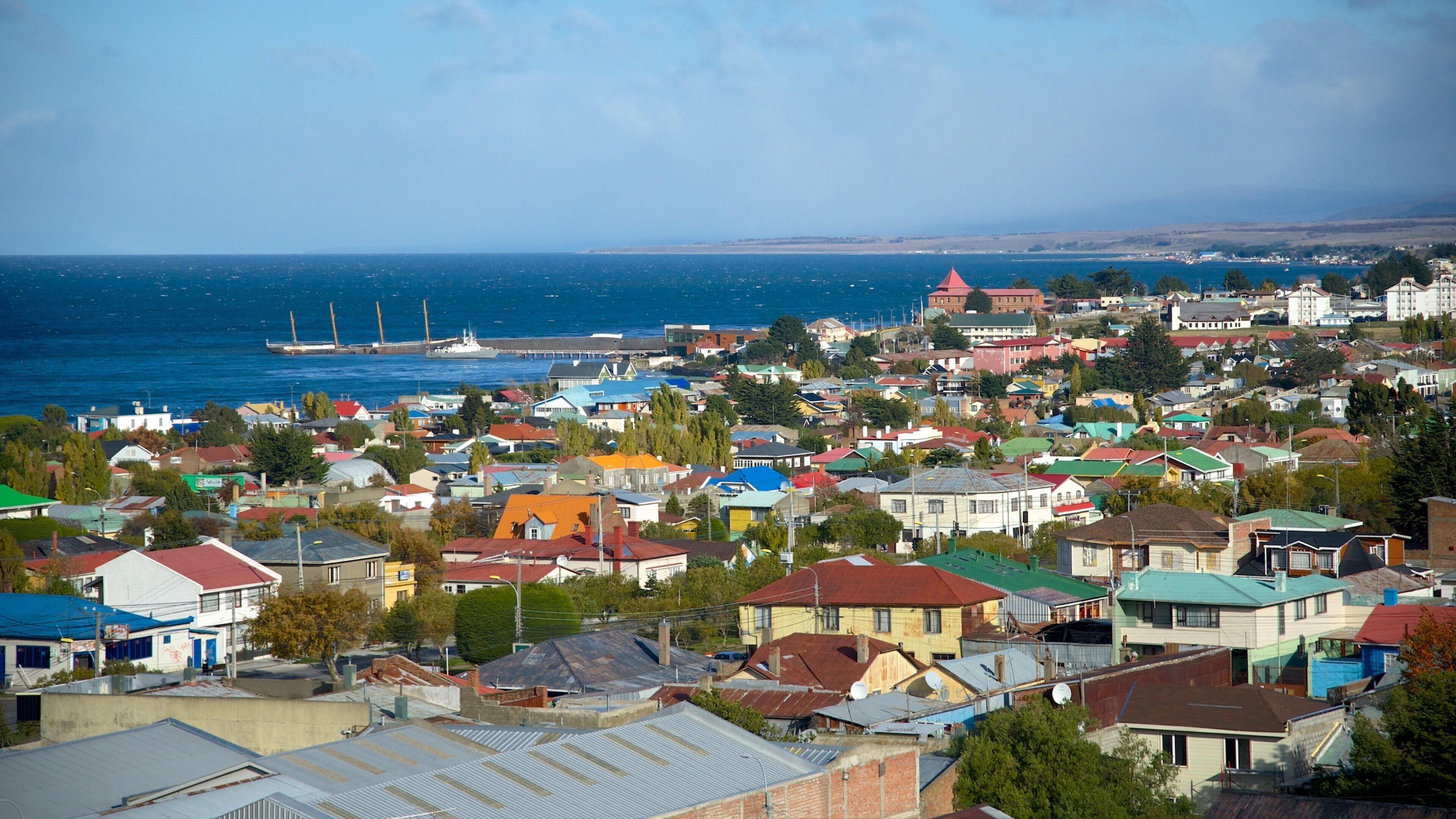 A coastal town with colorful houses, a harbor with ships, and a distant mountain range.