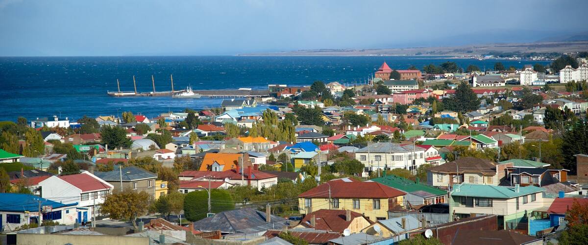 A coastal town with colorful houses, a harbor with ships, and a distant mountain range.
