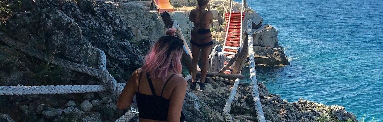 Uma trilha costeira rochosa com uma ponte de corda e um escorregador dando para o mar.