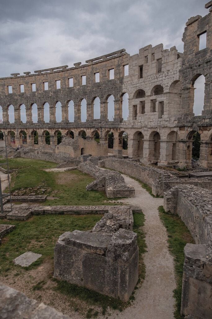 The most famous and important monument, the starting and ending point of every sightseeing tour is the Amphitheater, popularly called the Arena of Pula, which was once the site of gladiator fights. It was built in the 1st century AD during the reign of Emperor Vespasian, at the same time as the magnificent Colosseum in Rome.

The ground plan is elliptical, the longer axis measuring about 130 m and the shorter one about 100 m. Gladiator fights took place in the central flat area called the arena, while the spectators could sit on the stone tiers or stand in the gallery. It is believed that the Amphitheater could seat about 20,000 spectators. Local limestone was used for its construction. In the Middle Ages it was the site of knights tournaments and fairs.