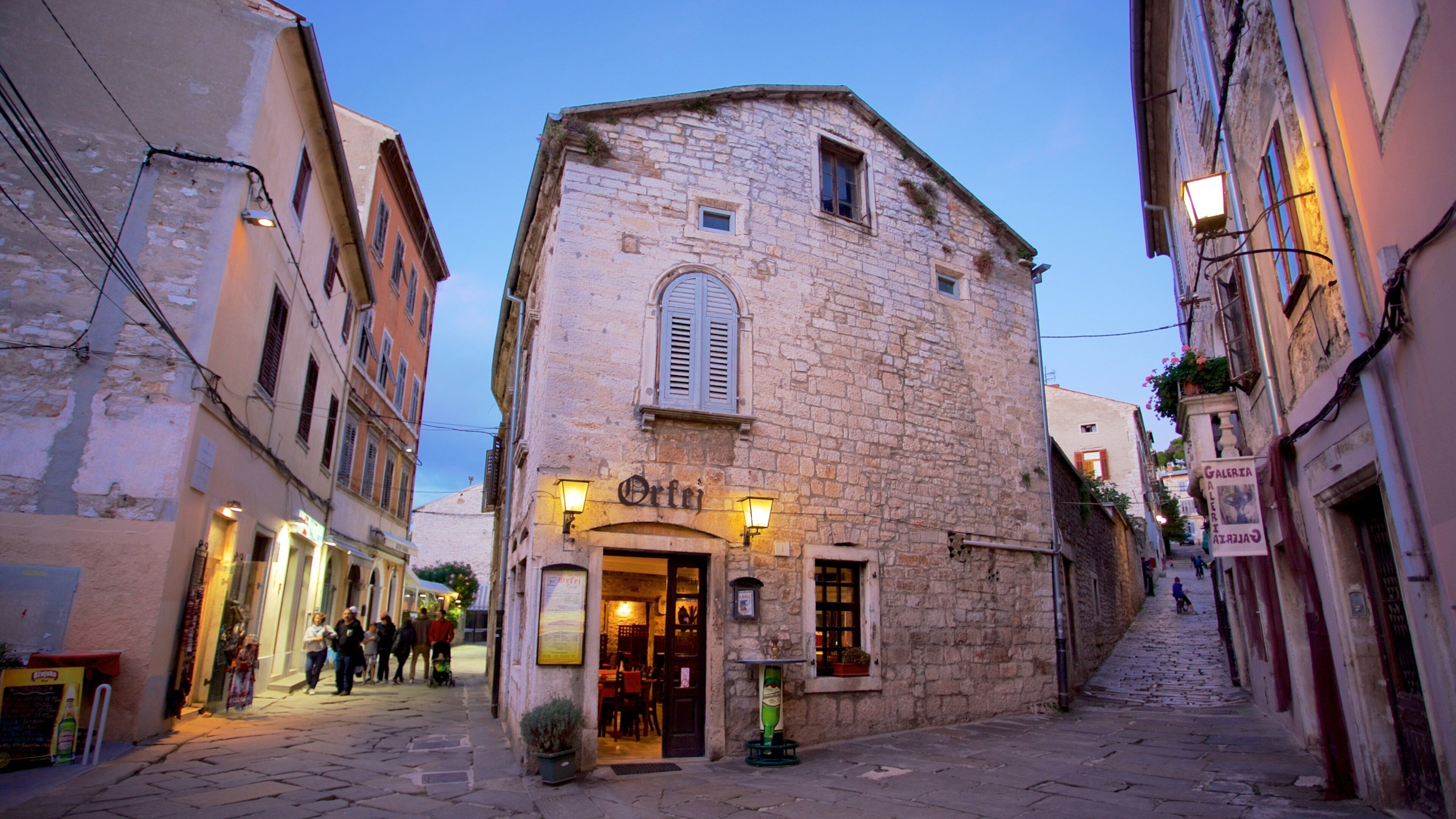 A narrow cobblestone street with historic stone buildings, a café named "Orte", and a sign for "Galeria".