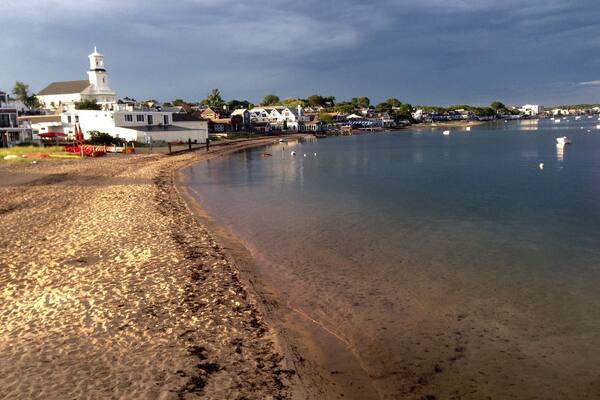 Ein Strand mit einem Leuchtturm, ruhigem Wasser und Häusern entlang der Küste.