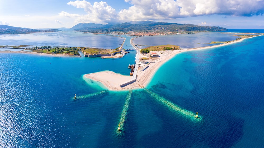 Eine Luftaufnahme einer Küstenlandschaft mit einer markanten Halbinsel, klarem, blauem Wasser und Bergen in der Ferne.