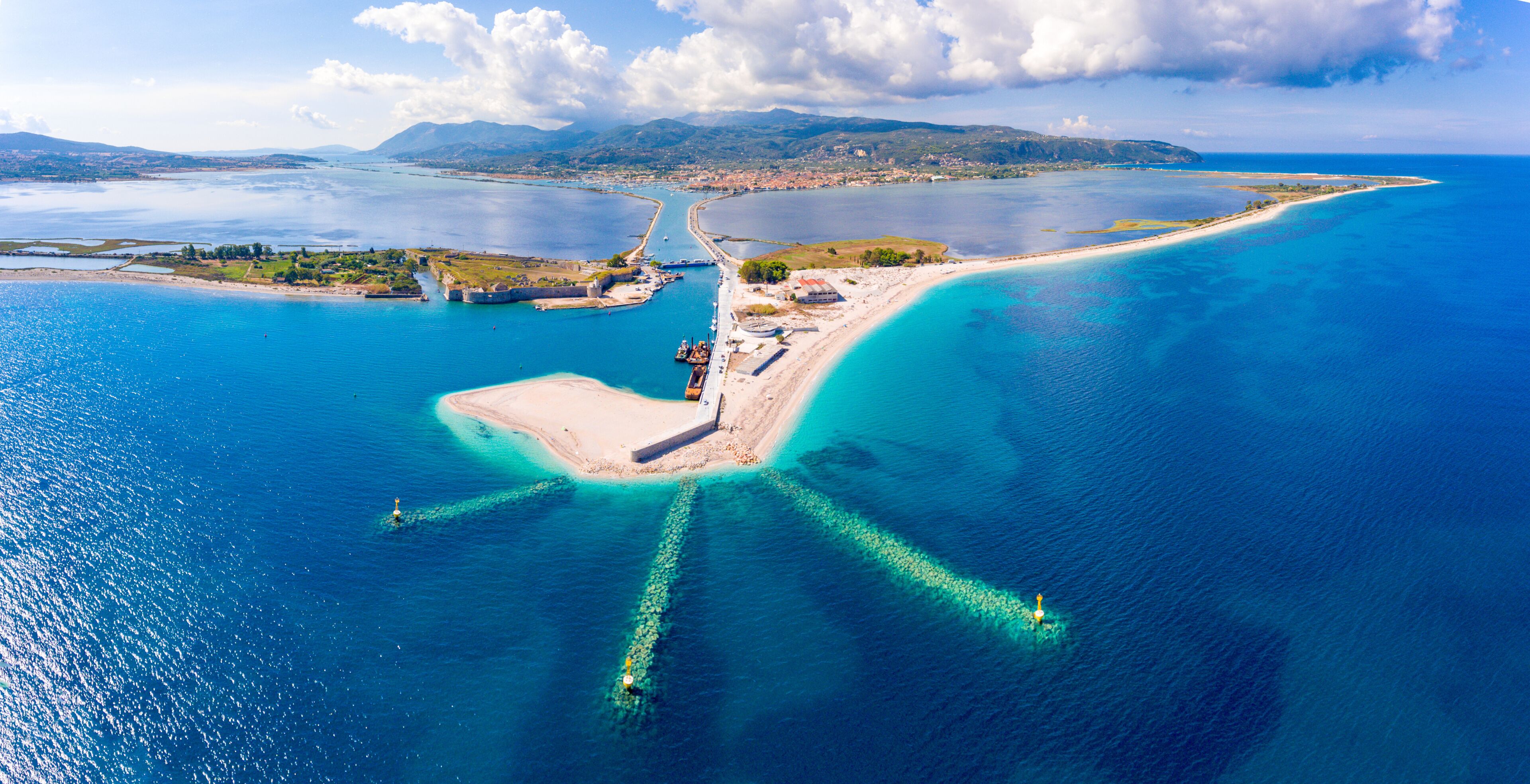 An aerial view of a coastal area with a prominent peninsula, clear blue waters, and distant mountains.