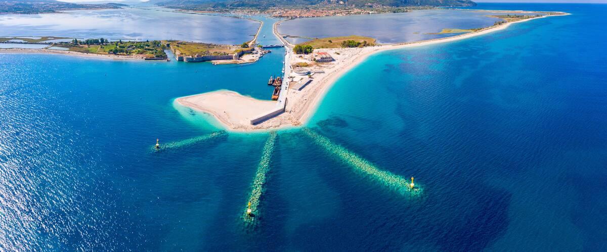 An aerial view of a coastal area with a prominent peninsula, clear blue waters, and distant mountains.