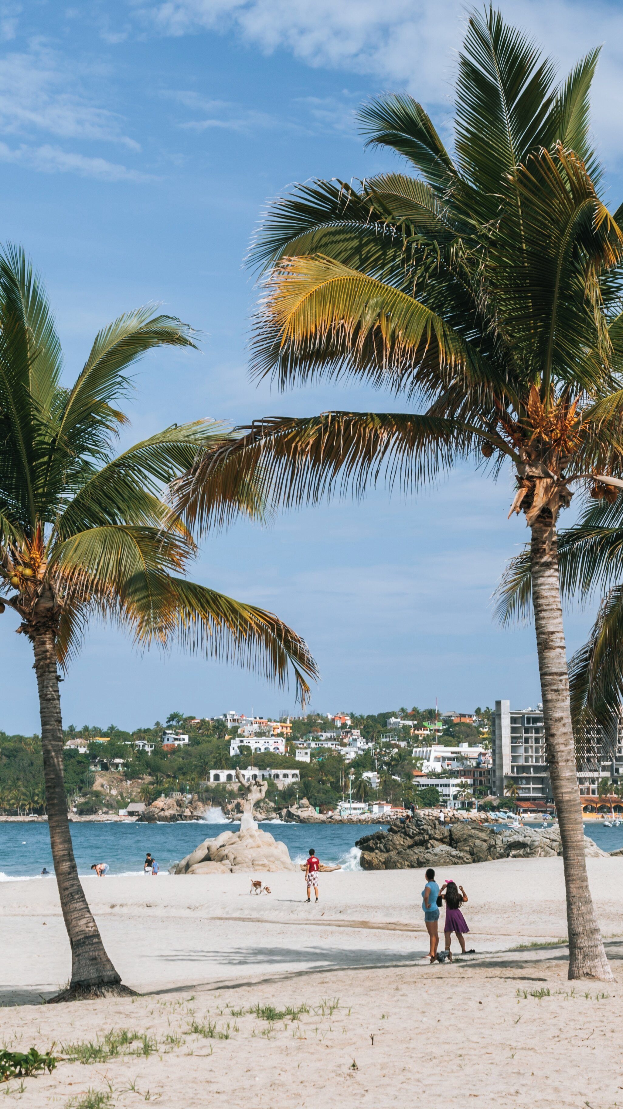 Warm sunny day at Zicatela Beach in Puerto Escondido, where visitors enjoy the sand and surf surrounded by palm trees