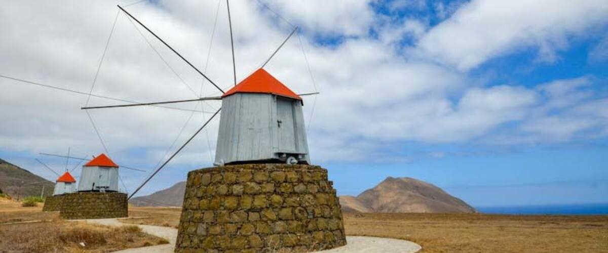 Windmills with red roofs in a grassy field with mountains in the background.