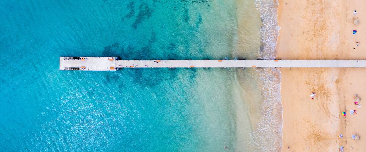 A pier extending into turquoise waters with a sandy beach and scattered beachgoers.