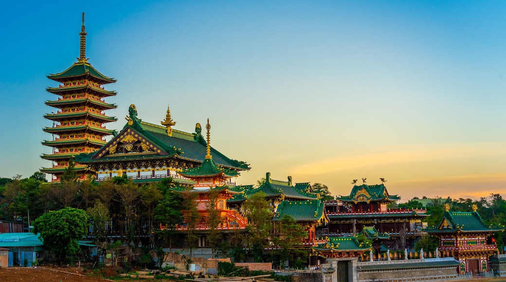 A traditional multi-tiered pagoda with ornate golden details, surrounded by lush greenery and other traditional buildings.