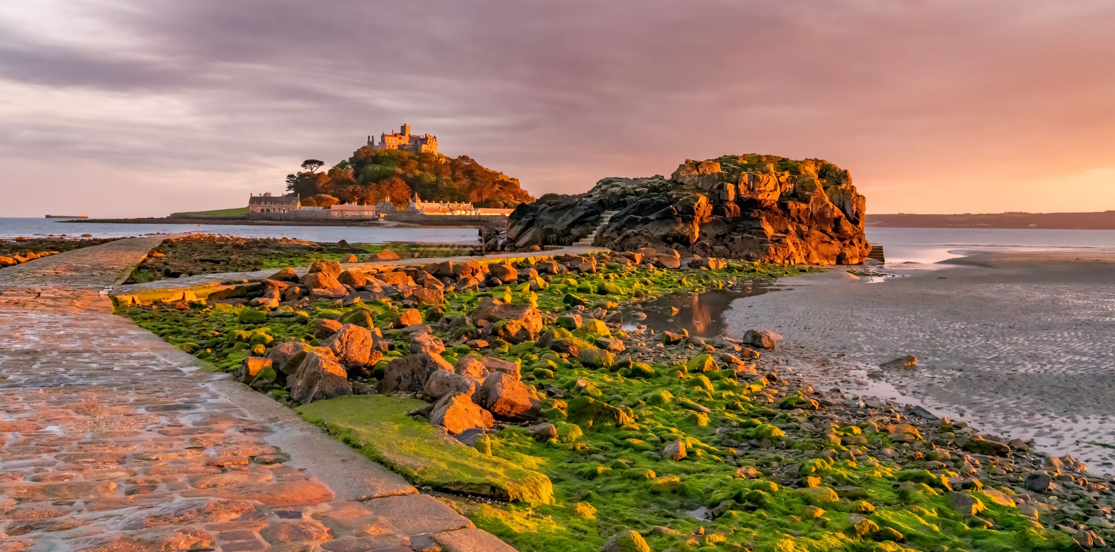 A coastal landscape with a castle on a hill, a rocky outcrop, and a stone pathway.