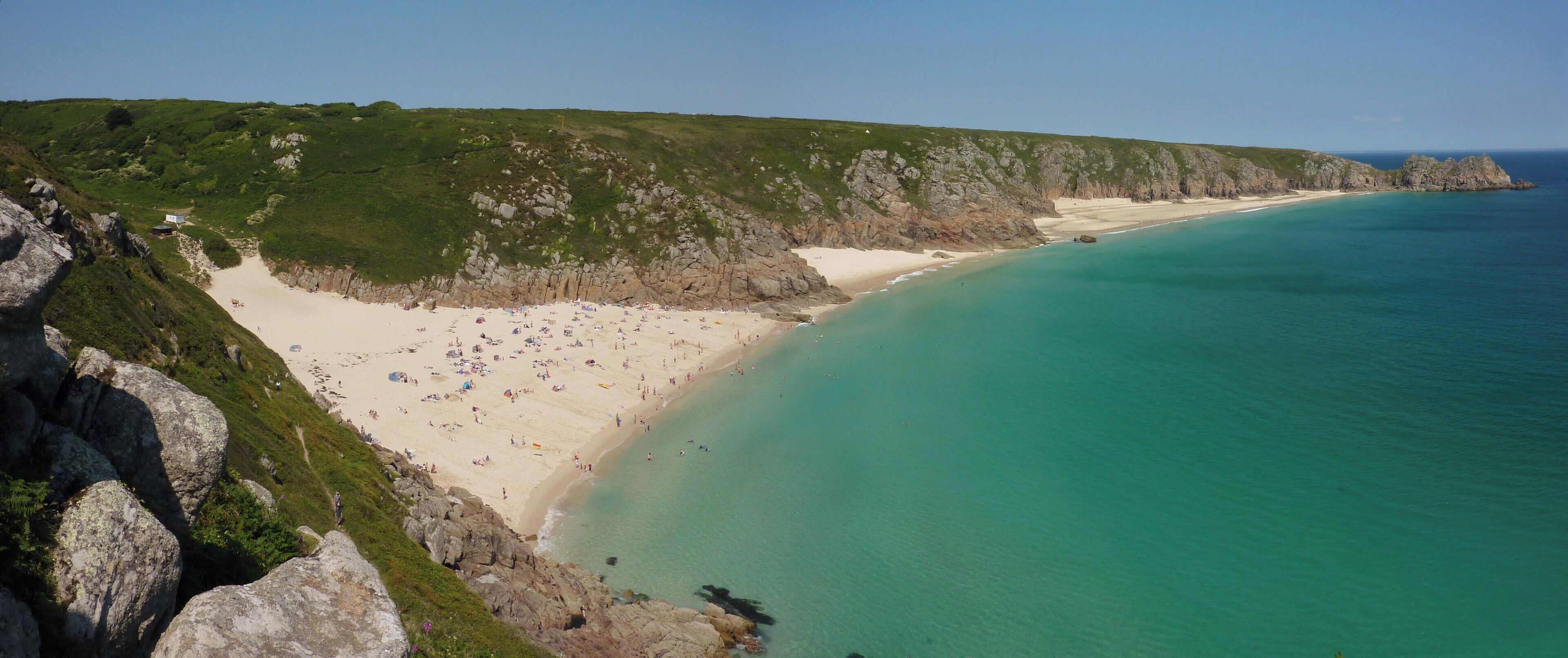 A coastal landscape with a sandy beach, rocky cliffs, and clear turquoise waters.