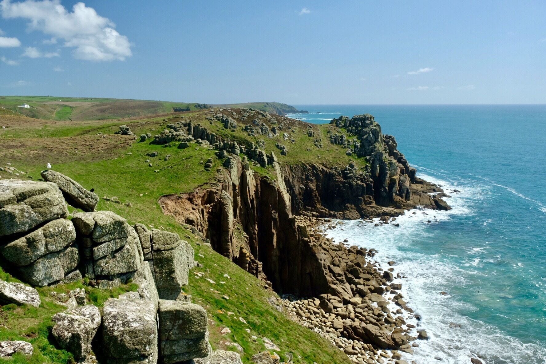 A coastal landscape with rocky cliffs, green hills, and the ocean.