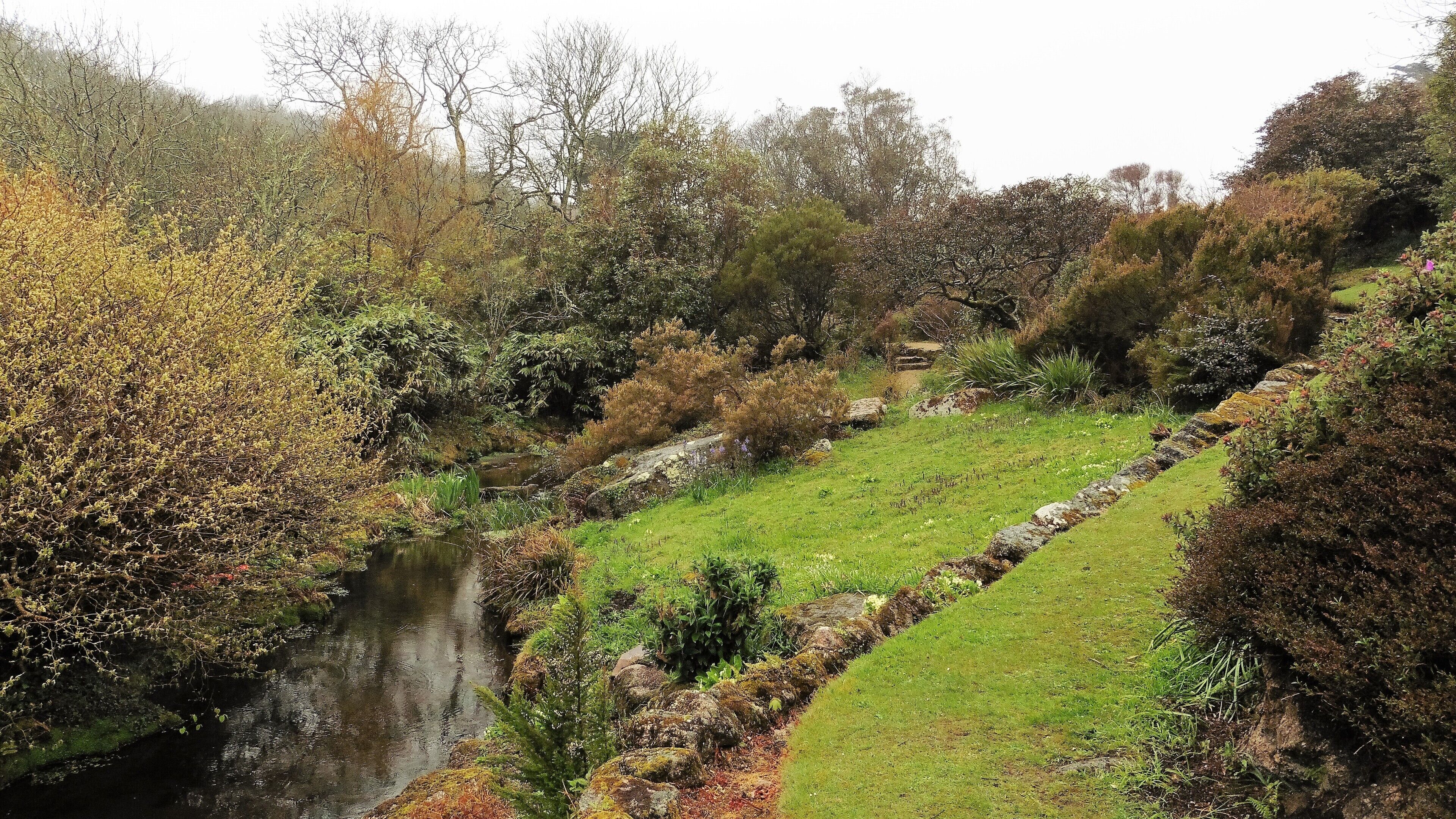 A river flowing through a valley with a stone wall and lush greenery.