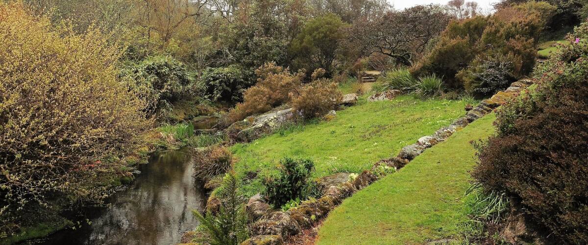 A river flowing through a valley with a stone wall and lush greenery.