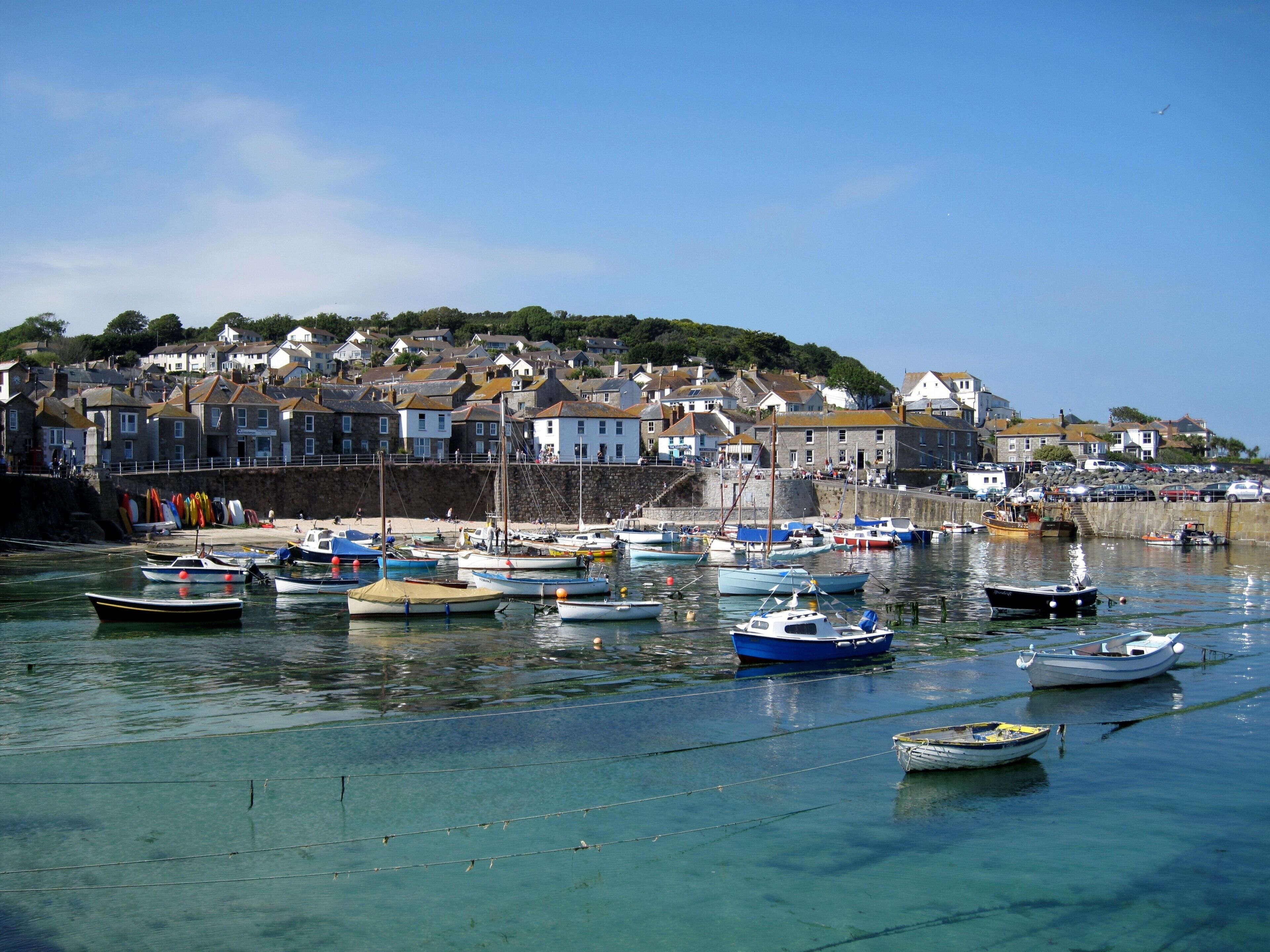 A harbor with various boats, a coastal town with houses, and clear blue water.