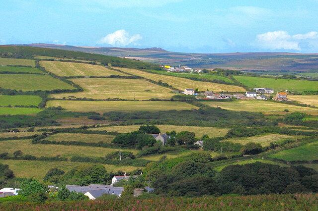 Rolling green hills, scattered houses, and distant mountains under a clear sky.