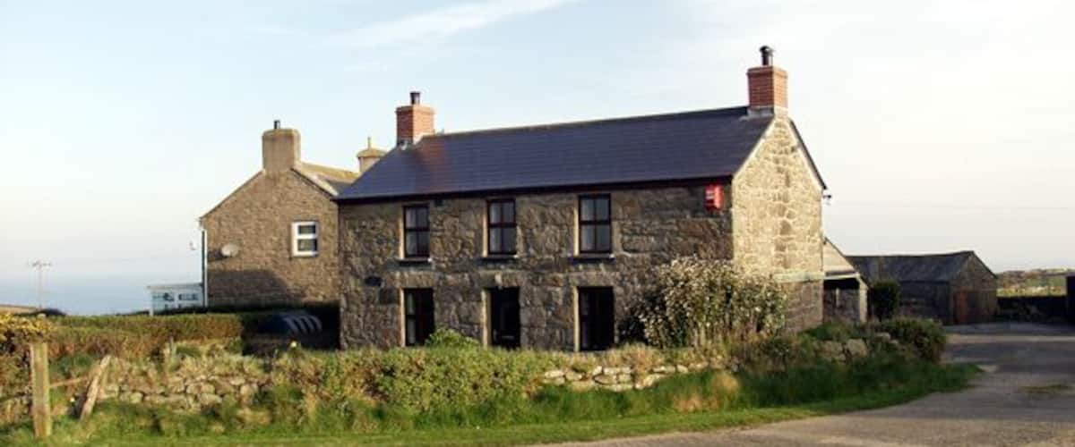 A stone house with a sloped roof and chimneys, surrounded by a grassy area and a paved path.