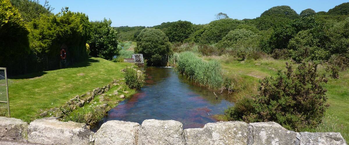 A river flowing through a rural landscape with stone walls and lush greenery.