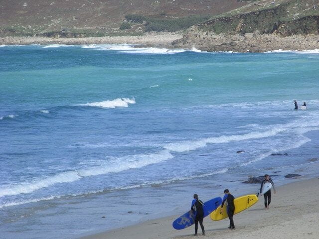 A beach with surfers walking along the shore carrying surfboards.
