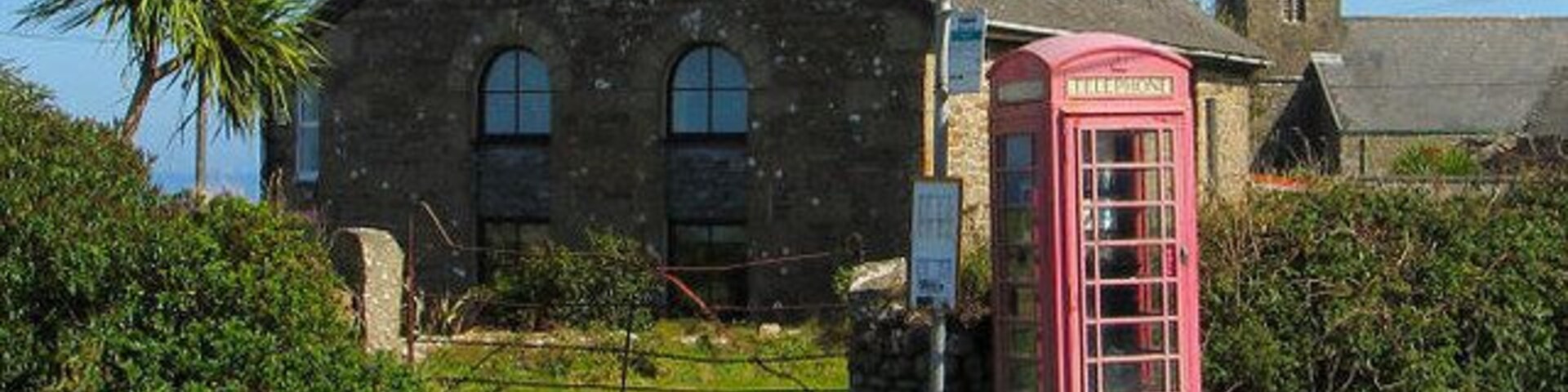Un edificio de piedra con una cabina telefónica roja e iglesia al fondo.