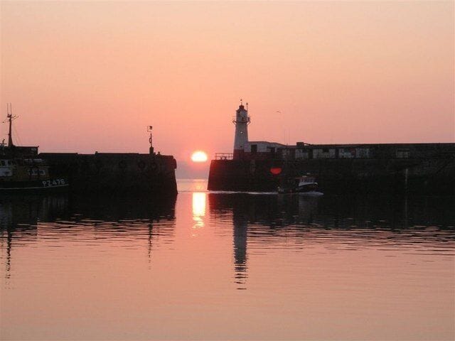 A sunset over a harbor with a lighthouse and a ship.