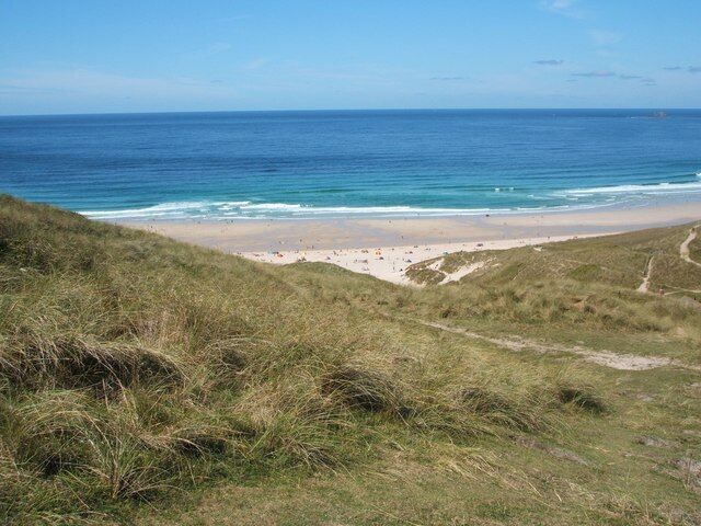 A beach with grassy dunes and a clear view of the ocean.
