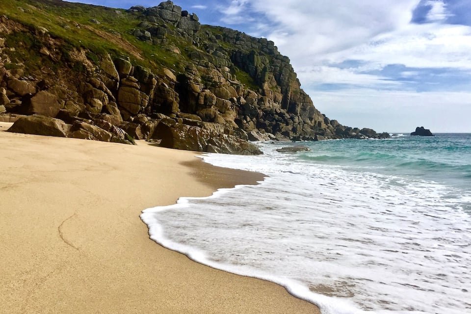 A sandy beach with gentle waves, rocky cliffs, and a clear sky.