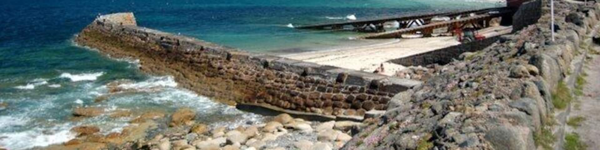 A rocky shoreline with a breakwater, calm sea, and a building in the distance.