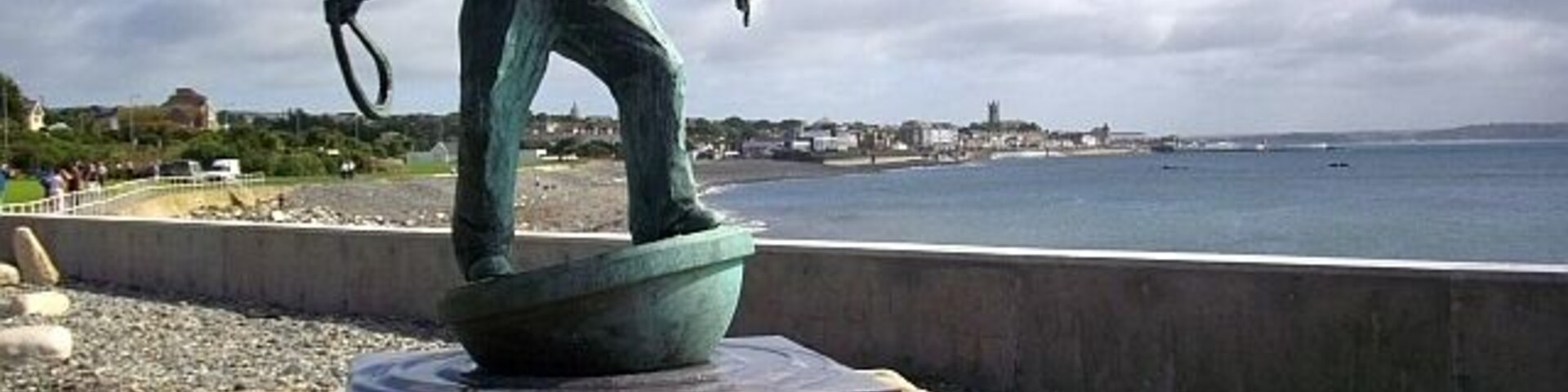 Una estatua de un hombre sosteniendo una caña de pescar sobre un pedestal, junto a la orilla del mar.