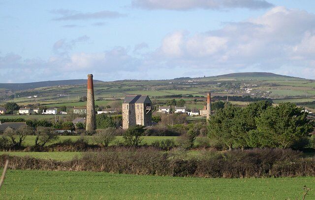 A rural landscape with a stone tower, two chimneys, and a small building.